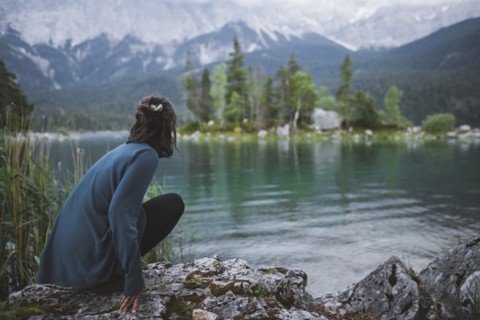 Germany, Bavaria, Eibsee, Young woman crouching on rock at shore of Eibsee lake in Bavarian Alps