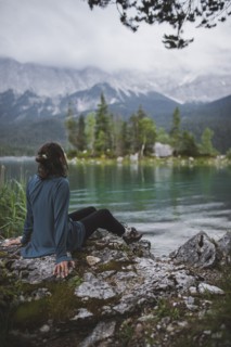 Germany, Bavaria, Eibsee, Young woman sitting on rock at shore of Eibsee lake in Bavarian Alps