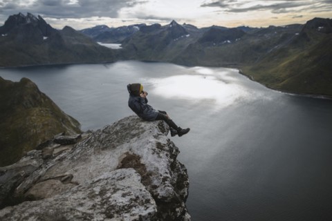Norway, Senja, Man taking photo sitting on edge of steep cliff on top of mountain Segla