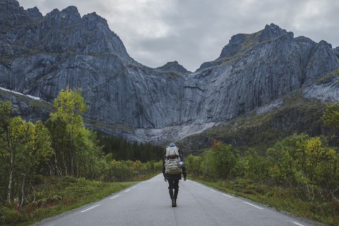 Norway, Lofoten Islands, Backpacker walking down road in mountain landscape