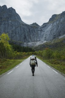 Norway, Lofoten Islands, Backpacker walking down road in mountain landscape