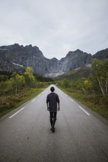 Norway, Lofoten Islands, Man walking down road in mountain landscape