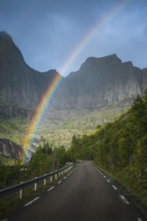 Norway, Lofoten Islands, Rainbow above empty road in mountain landscape