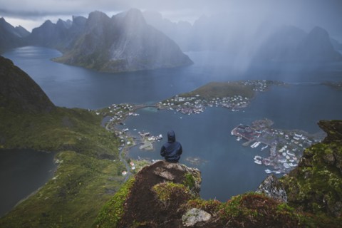 Norway, Lofoten Islands, Reine, Man looking at fjord from Reinebringen mountain during rain