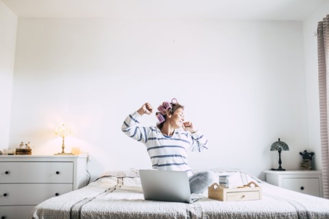 Woman sitting on bed with laptop and stretching