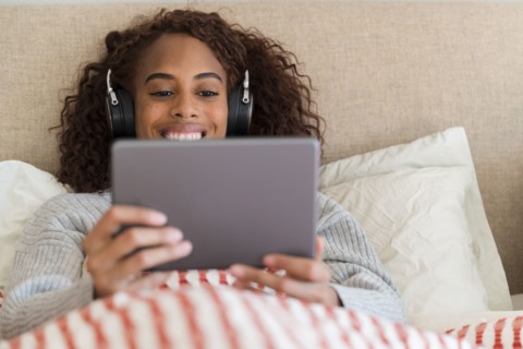 Smiling woman using tablet with headphones in bed