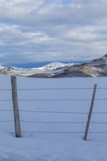 Barbed wire fence in snow with mountains in distance