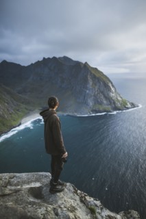 Man holding camera on cliff at Ryten mountain in Lofoten Islands, Norway