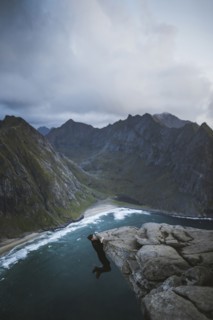 Man hanging on cliff at Ryten mountain in Lofoten Islands, Norway