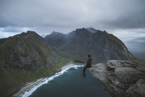 Man sitting on cliff at Ryten mountain in Lofoten Islands, Norway
