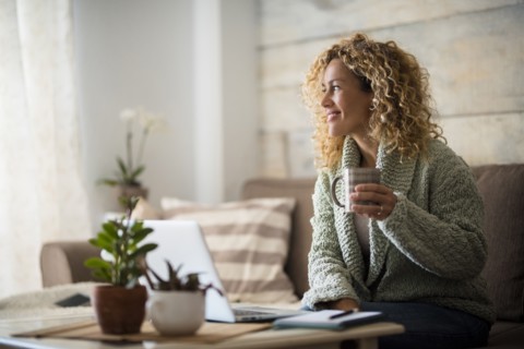 Smiling woman holding drink at laptop
