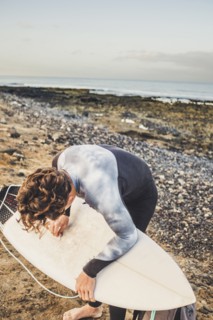 Teenage boy waxing surfboard at beach