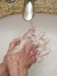 Senior woman washing hands in bathroom sink, close-up of hands