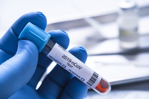 Close-up of gloved hand holding test vial labelled 2019-nCoV