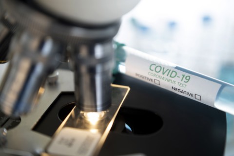 Laboratory microscope with a slide and vial of coronavirus test
