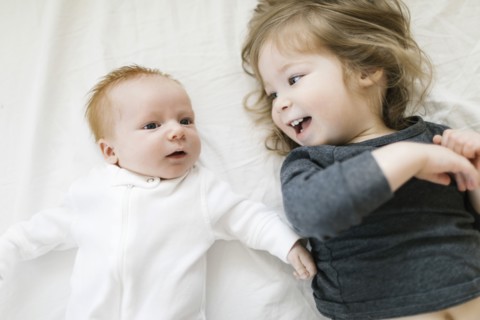 Siblings (2-5 months, 2-3) lying on bed