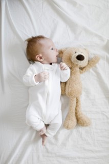 Baby boy (2-5 months) lying on bed with teddy bear