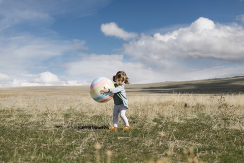 Girl (2-3) holding ball in open field