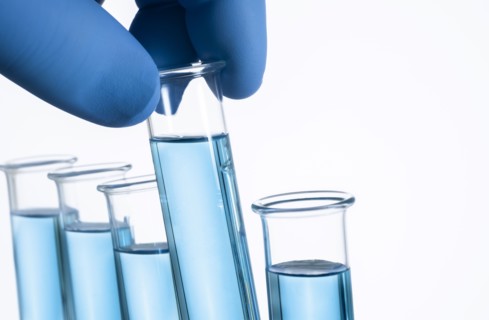 Fingers in blue latex glove holding test tube with liquid