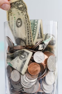 Close-up of fingers pulling one dollar bill from jar with American cents and banknotes