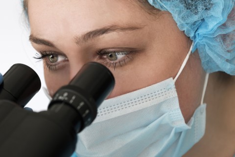 Laboratory technician in face mask looking through microscope
