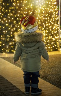 Boy in Christmas hat watching illuminated Christmas tree