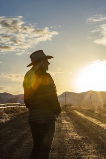 USA, Idaho, Sun Valley, Woman in cowboy hat standing on dirt road at sunset