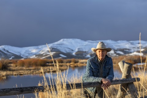 USA, Idaho, Sun Valley, Senior man in cowboy hat leaning against fence