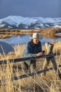 USA, Idaho, Sun Valley, Senior man in cowboy hat leaning against fence
