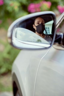 Woman with face mask driving car reflected in mirror