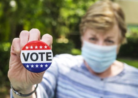 Portrait of woman wearing surgical mask holding Vote button