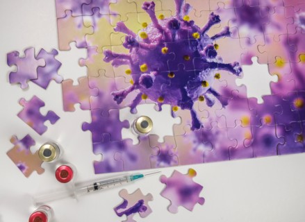 Studio shot of puzzle with Coronavirus model and vaccine vials and syringe