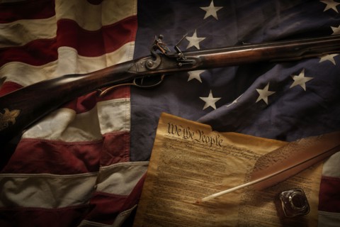 Rifle and US constitution lying on American flag