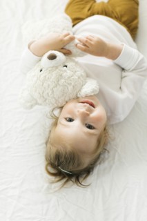 Smiling toddler girl lying on bed with teddy bear toy