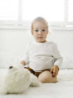 Smiling toddler girl sitting on bed with teddy bear toy