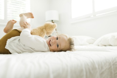 Toddler girl lying on bed with her teddy bear toy