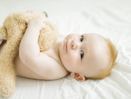 Portrait of baby boy lying on bed with teddy bear