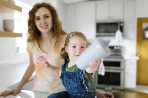 Girl (2-3) sitting on kitchen counter next to mother and holding sippy cup