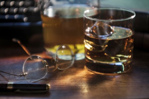 Whiskey glass and eyeglasses next to typewriter on desk