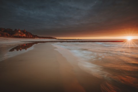 Poland, Pomerania, Leba, Baltic Sea coastline with distant town at sunset