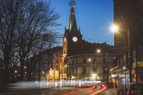 Poland, Lesser Poland, Krakow, Illuminated city street with clock tower at night