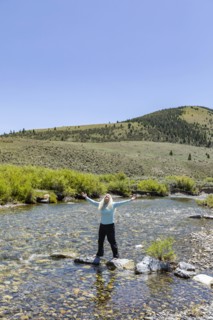USA, Idaho, Sun Valley, Woman with arms raised standing on rocks in river