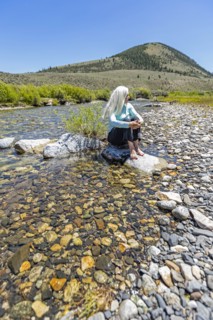 USA, Idaho, Sun Valley, Woman sitting on rock in river