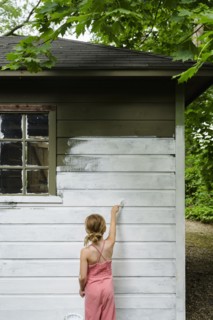 Girl (6-7) painting cottage wall
