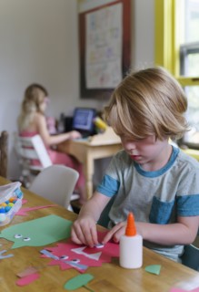 Boy (4-5) preparing paper cutout, girl (6-7) in background