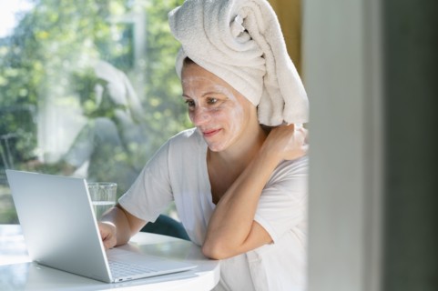 Woman with face mask and towel on head using laptop at table