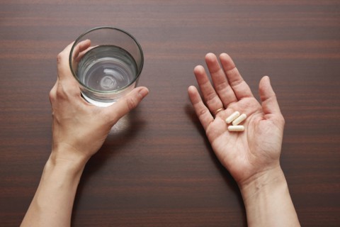 Woman's hands holding pills and glass of water