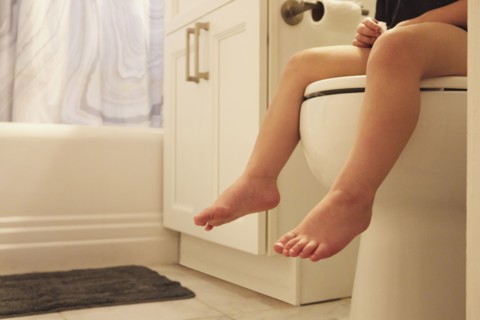 Legs of toddler girl (2-3) sitting on toilet seat