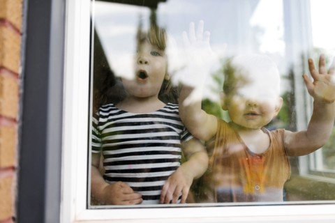 Portrait of toddler girl (2-3) and baby boy (18-23 months) standing behind window