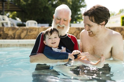 Grandfather, son and grandson (2-3) standing in outdoors swimming pool